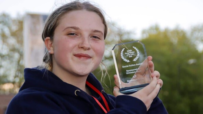 Young person holding a glass award trophy outdoors, smiling at camera, wearing navy hoodie with red lanyard