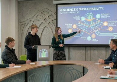 Young person presenting a Resilience and Sustainability long-term plan to adults in a boardroom setting