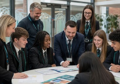 Teachers and secondary school students reviewing materials around a table in a bright school atrium