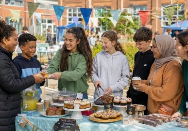 Young people serving food at an outdoor school bake sale fundraiser decorated with bunting